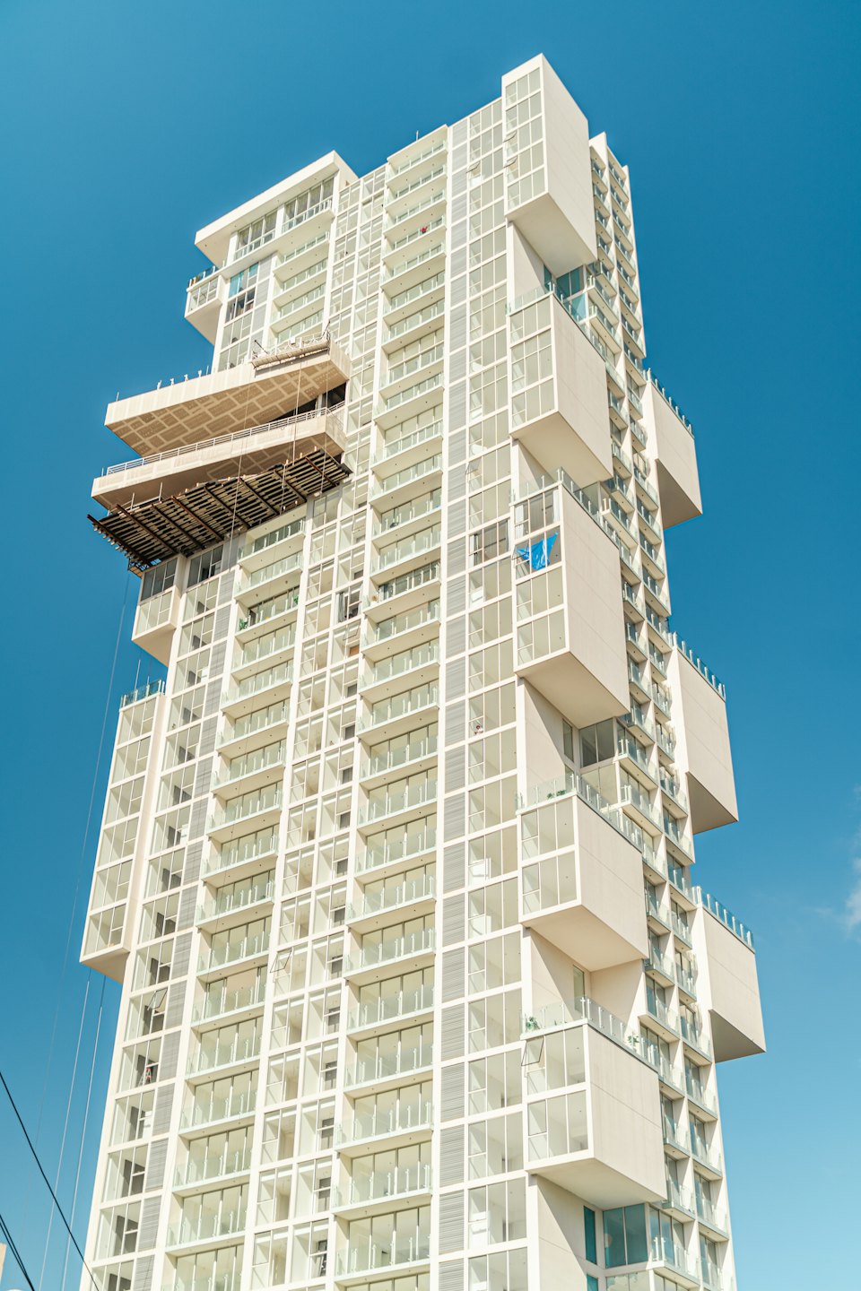 Mavi gökyüzüne karşı iskeleli modern beyaz apartman binası.