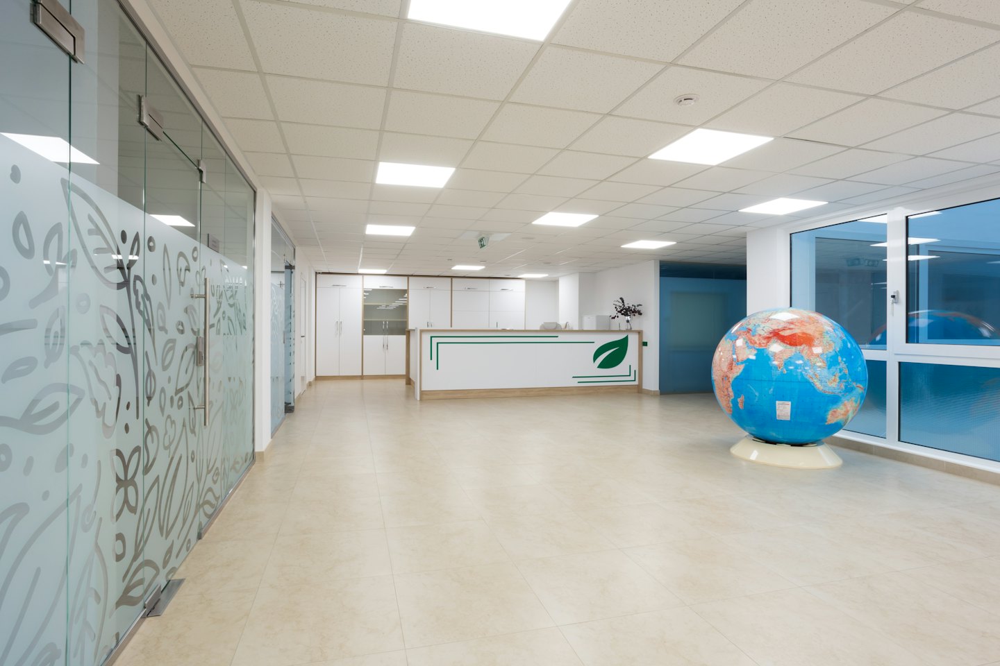 Modern ofis resepsiyon masası, üzerinde dünya küresi ve buzlu cam bölmeler.